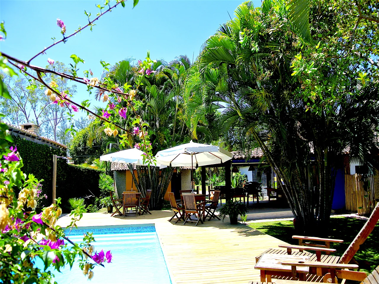 Piscina, jardim e mesas com guarda-sol da Pousada El Capitan