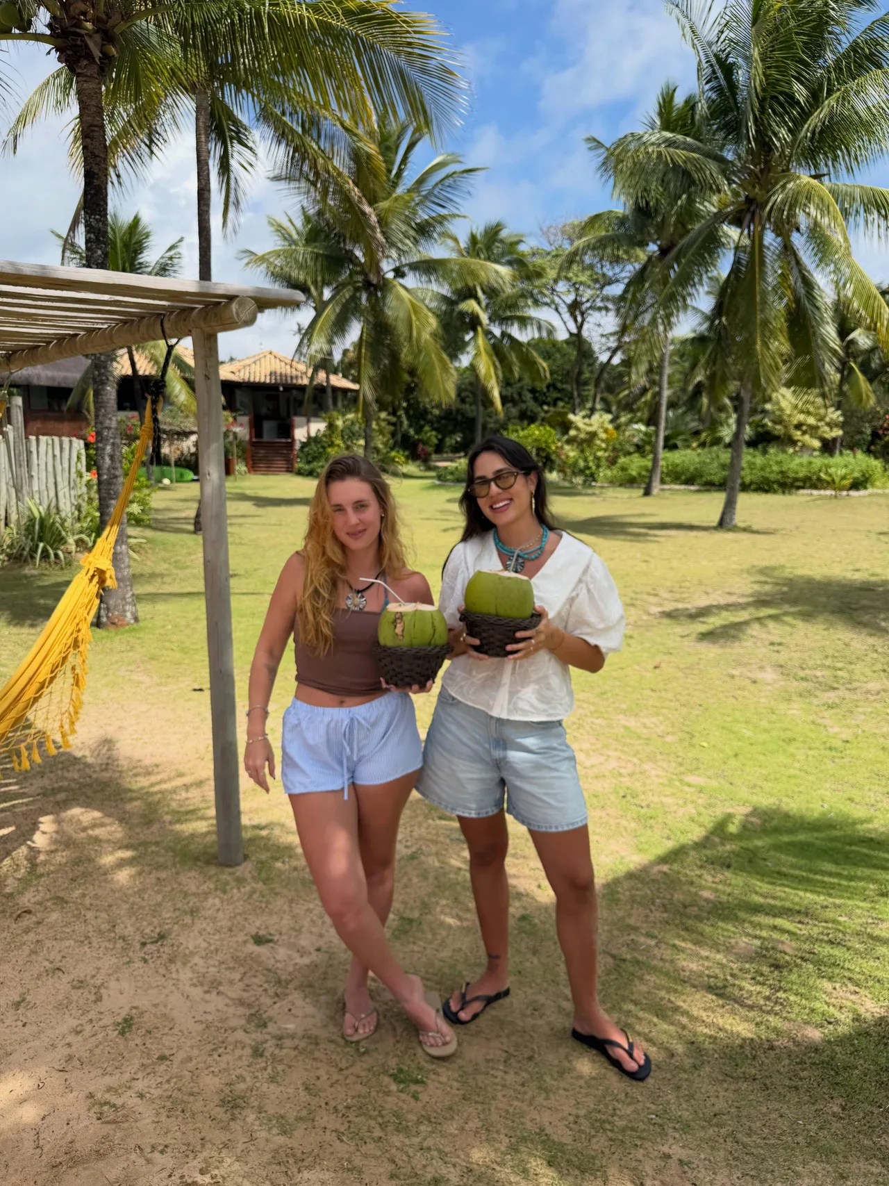 Duas pessoas segurando cocos no jardim da Pousada Lagoa do Cassange